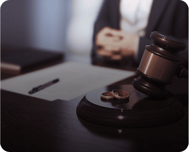 Wooden table with a gavel and two wedding rings on top of it, along with a pen and a book